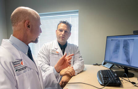 Mitchell Carl, MD and James Kalmuk, MD, sit at a desk in front of a screen showing lung imaging