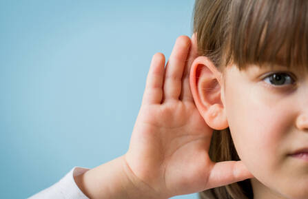 A child holder her hand up to her left ear