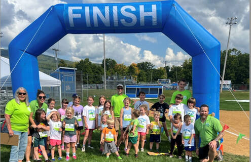 A group of Health Kids Running kids and adult volunteers standing under a "Finish" archway