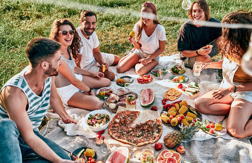 A group of people sitting on a picnic blanket filled with food