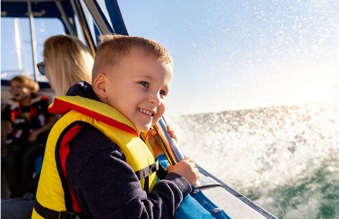 A smiling child in a life jacket riding in a boat